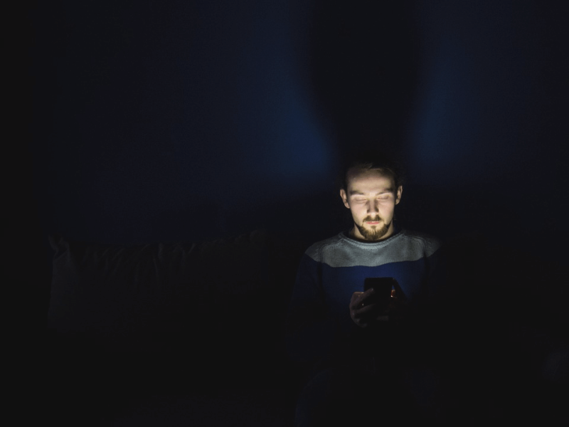 man with face illuminated by smartphone screen in a dark room