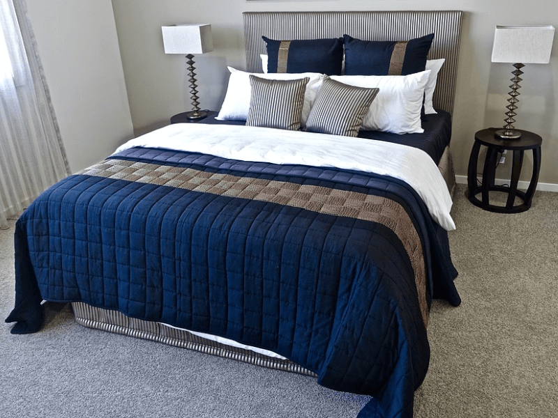 A bed with dark blue beddings and an assortment of pillows
