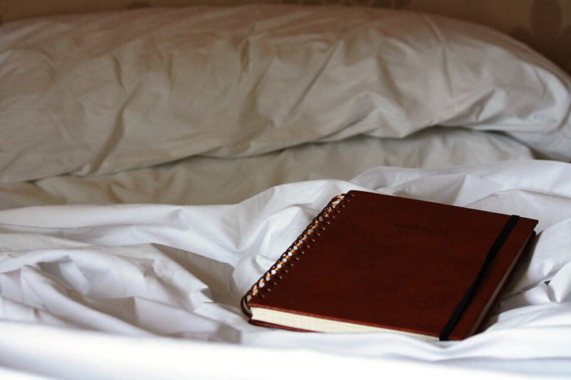 brown ring bound notebook on bed with white sheets