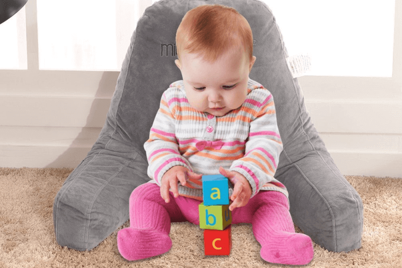 baby in striped shirt and pink tights playing with alphabet blocks and leaning on gray mittaGonG Backrest husband pillow