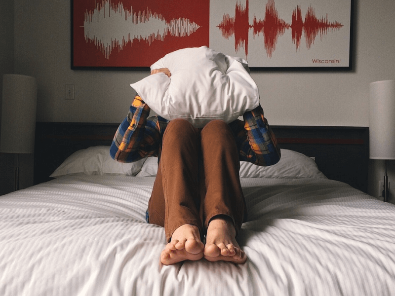 A person on a bed covering their face with a pillow