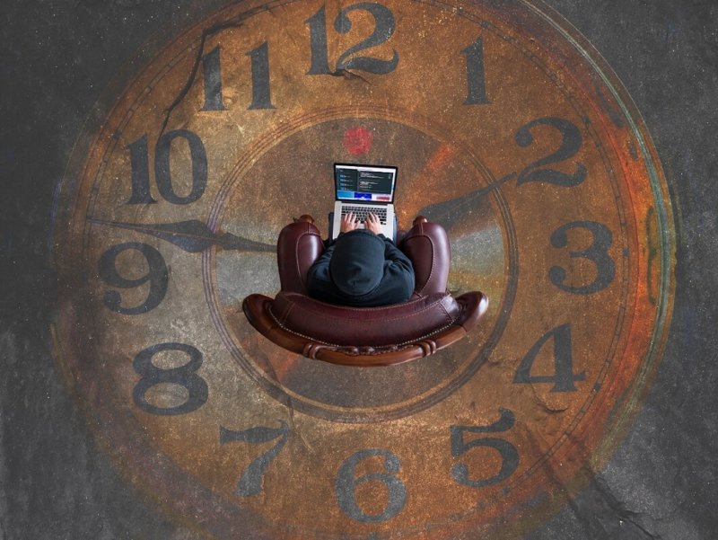 Person sitting with laptop amidst large clock face