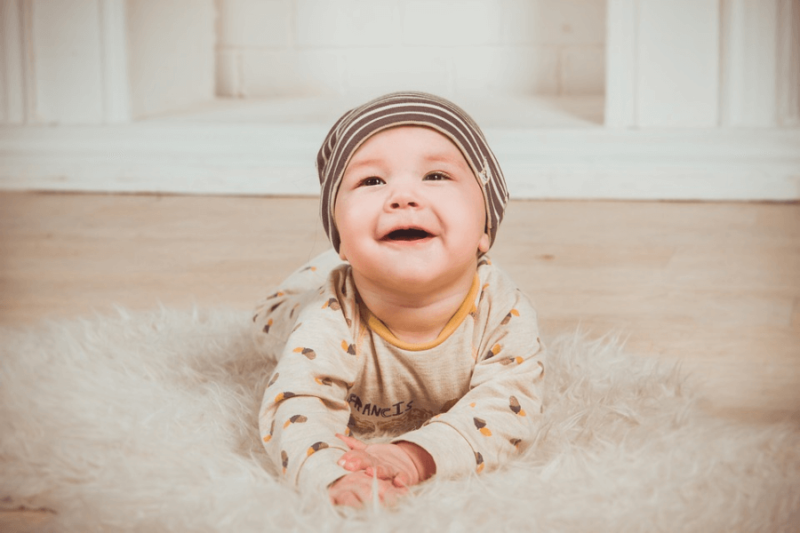 A smiling baby with a bonnet on a rug